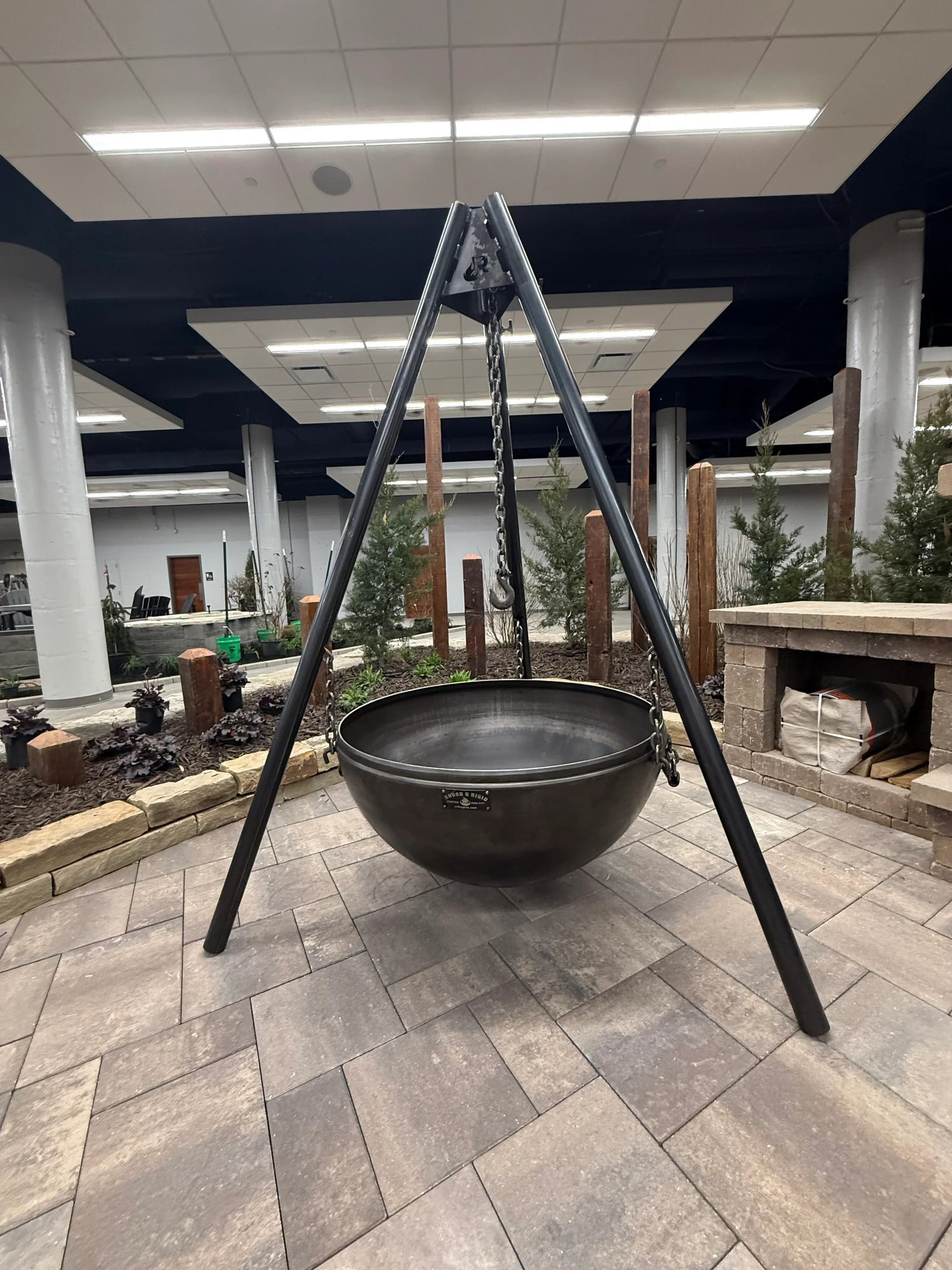 A large 40-inch hanging cauldron-style fire pit with a tripod made from carbon steel, displayed indoors.